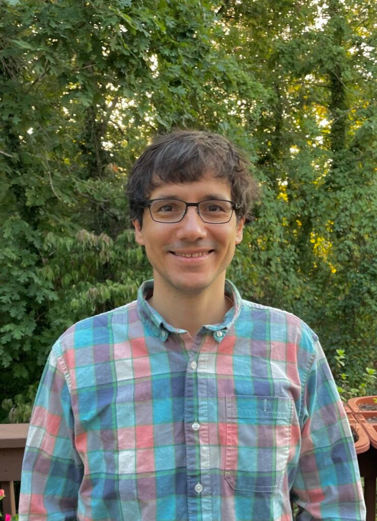 Mauro standing in front of greenery, smiling.